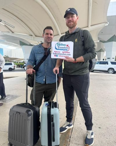 Grupo de amigos de pie en la terminal con maletas, sosteniendo el banner de Holbox Transfers antes de su viaje a Holbox.