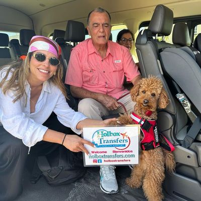 Una familia feliz sostiene el banner de Holbox Transfers dentro de la van junto a su perrito, camino a Holbox.