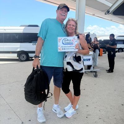 Viajeros felices abrazados en la acera de la terminal, mostrando el banner de Holbox Transfers mientras esperan partir a Holbox.