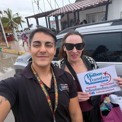 Viajeros felices posan para una selfie con el banner de Holbox Transfers en el muelle, celebrando su llegada cerca de la isla de Holbox.