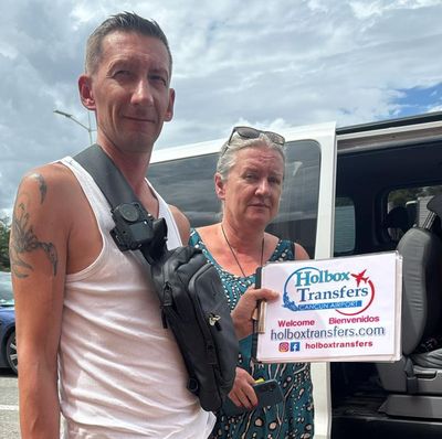 Viajeros felices de pie junto a la van sostienen el banner de Holbox Transfers, en una pausa durante el traslado Aeropuerto de Cancún - Holbox.