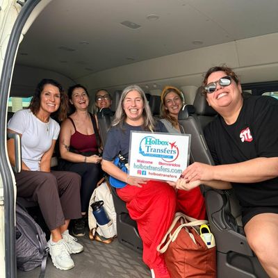 Un grupo grande de amigos llena la van, sonriendo y riendo mientras uno sostiene el banner de Holbox Transfers rumbo a Holbox.
