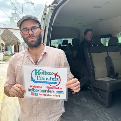 Pareja sonriente aborda la van en una calle tranquila, sosteniendo el banner de Holbox Transfers antes del trayecto a Holbox.