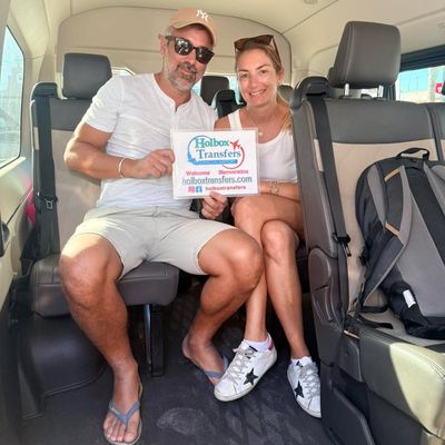 Una pareja sonriente sostiene el banner de Holbox Transfers dentro de la van, relajados y listos para el trayecto a Chichén Itzá.