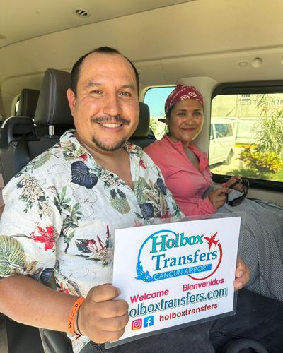Una pareja sonriente sostiene el banner de Holbox Transfers sentada dentro de la van, ya en camino rumbo a Holbox.