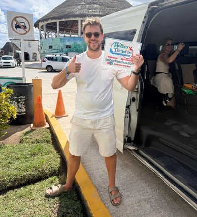 Pareja sonriente posa junta en la puerta abierta de la van, mostrando con orgullo el banner de Holbox Transfers antes de partir a Holbox.