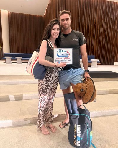 Pareja sonriente posa en el lobby de su destino con el banner de Holbox Transfers, relajados tras su traslado Aeropuerto de Cancún - Holbox.
