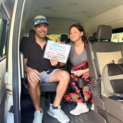 Pareja sonriente sentada junta dentro de la van, sosteniendo el banner de Holbox Transfers mientras comienza su trayecto a Holbox.