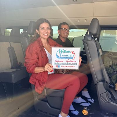 Pareja sonriente sentada dentro de la van sostiene el banner de Holbox Transfers, a medio camino del traslado Aeropuerto de Cancún - Holbox.
