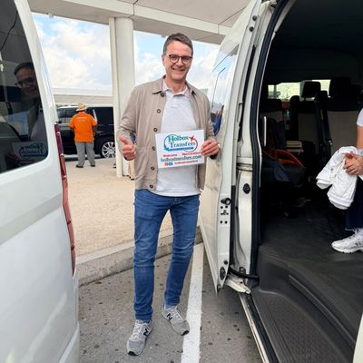 Viajero solo levanta el pulgar junto a la van, sosteniendo el banner de Holbox Transfers para el traslado Aeropuerto de Cancún - Holbox.