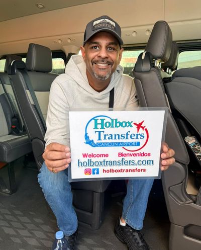 Viajero solo sosteniendo el banner de Holbox Transfers dentro de la van, sonriendo antes de la salida en la ruta Aeropuerto de Cancún - Holbox.