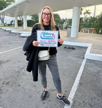 Un viajero solo sostiene el banner de Holbox Transfers en la terminal del aeropuerto, listo para comenzar la travesía a Holbox.