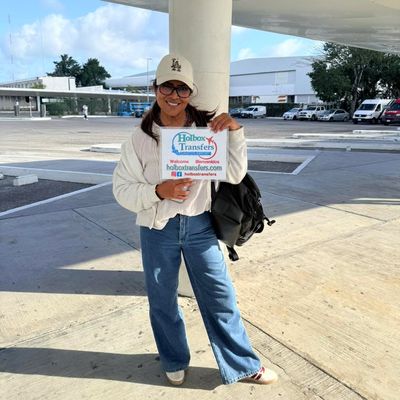 Viajero solo sonríe en la terminal del aeropuerto sosteniendo el banner de Holbox Transfers, esperando comenzar el traslado Aeropuerto de Cancún - Holbox.