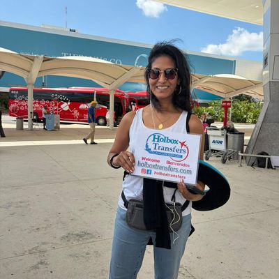 Viajero solo sonríe sosteniendo el banner de Holbox Transfers afuera de la terminal del aeropuerto antes del traslado Aeropuerto de Cancún - Holbox.