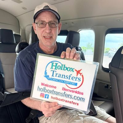 Viajero solo sonríe dentro de la van, sosteniendo en alto el banner de Holbox Transfers en su funda protectora antes de partir a Holbox.