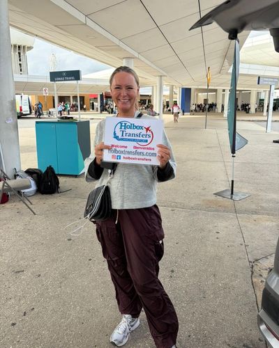 Viajero solo sonríe sosteniendo el banner de Holbox Transfers en la acera del Aeropuerto de Cancún antes de partir a Holbox.