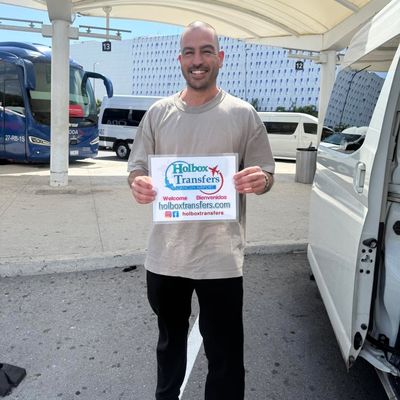Viajero solo sonriendo y sosteniendo el banner de Holbox Transfers en la terminal del aeropuerto antes de salir hacia Holbox.