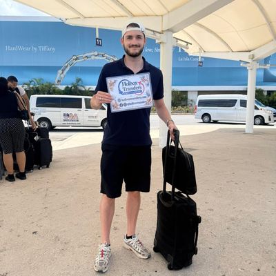 Viajero solo sonriendo en la terminal, sosteniendo el banner de Holbox Transfers junto a su equipaje antes del trayecto a Holbox.