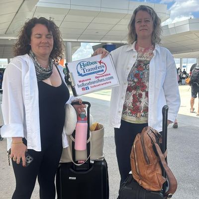 Dos amigos sostienen el banner de Holbox Transfers junto a su equipaje en la terminal, comenzando su traslado del Aeropuerto de Cancún a Holbox.