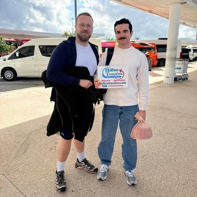Dos amigos sostienen juntos el banner de Holbox Transfers en la terminal del aeropuerto, a punto de partir a Holbox.